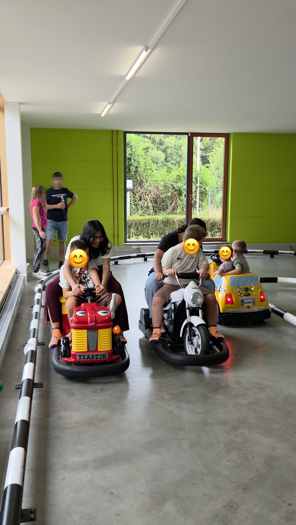Zwei Au-pairs fahren mit den Kindern der Gastfamilie auf einer Indoor-Fahrzeugbahn; die Gesichter der Kinder sind abgedeckt.