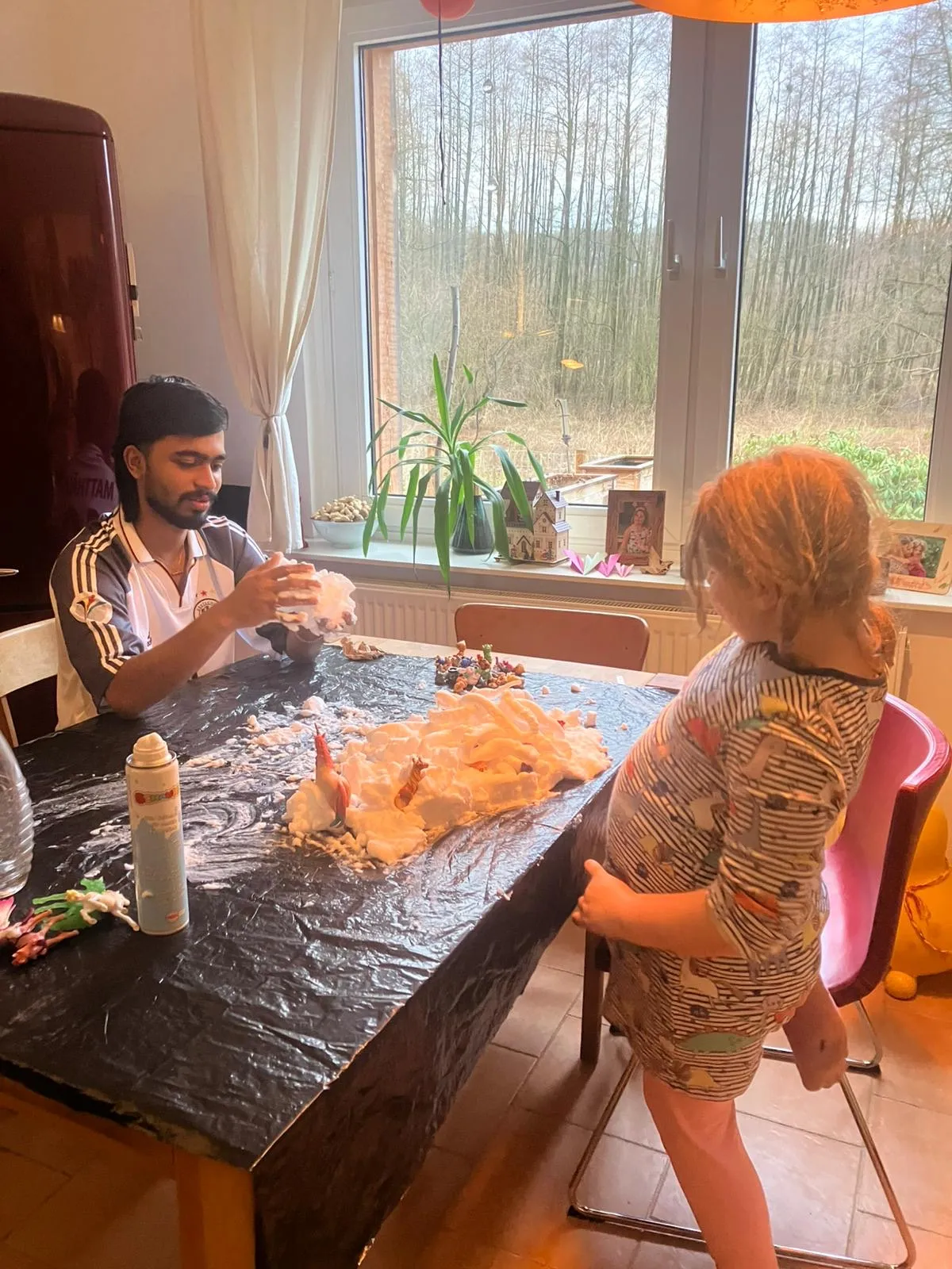 Au-pair und Mädchen bauen mit Rasierschaum eine Schneelandschaft am Fenster