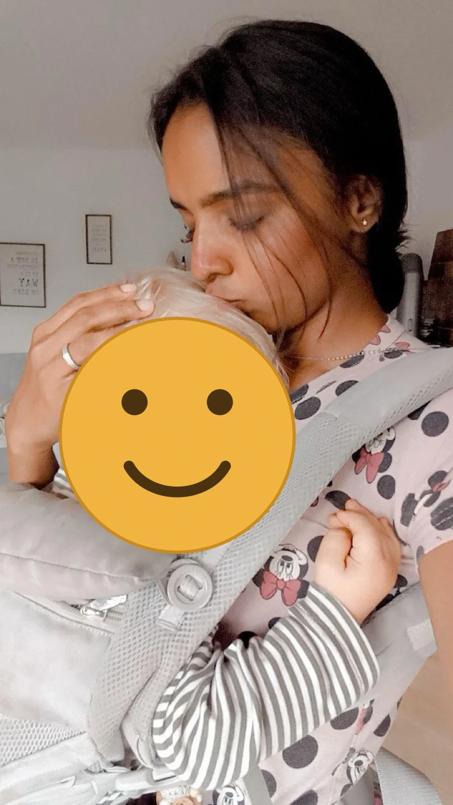 Au-pair küsst zart den Kopf eines schlafenden Kleinkinds in der Babytrage