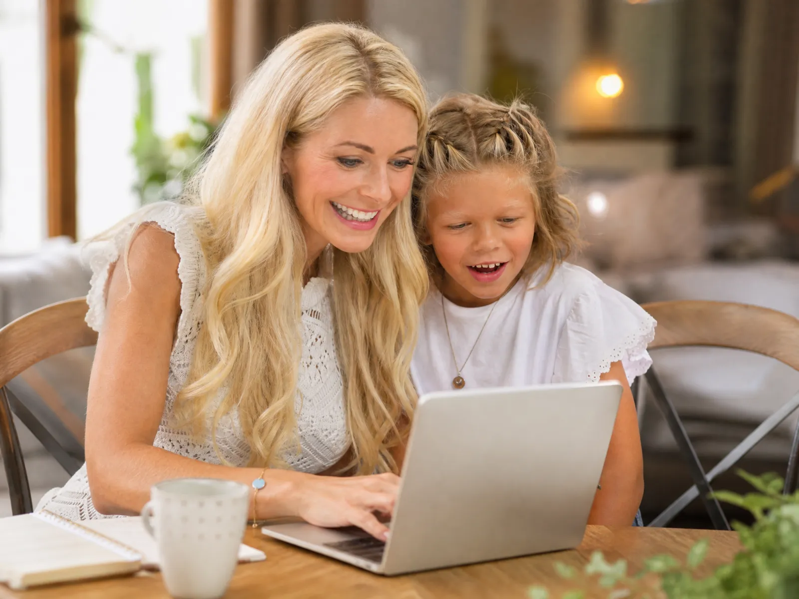 Eine Mutter sitzt mit ihrer Tochter am Küchentisch, beide schauen gemeinsam auf den Laptop.