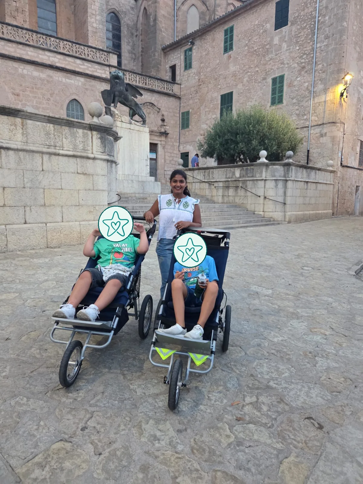 Ein Au-pair mit zwei Kindern in Reha-Buggys vor einer Kirche.